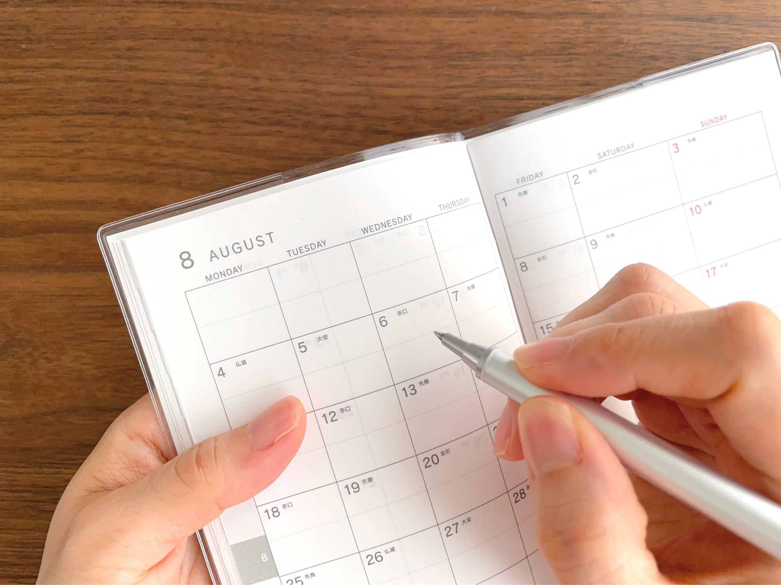 8月のスケジュール帳に記入する女性の手元